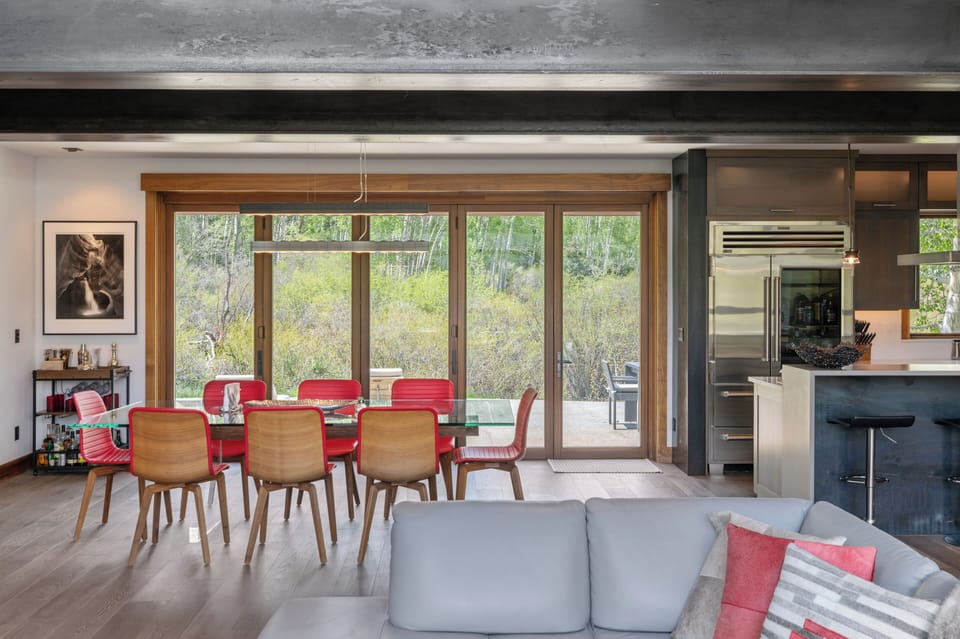 Spacious dining table with serene aspen tree views through floor-to-ceiling glass doors. Open-concept space flowing from modern kitchen to cozy living area creates an inviting atmosphere for memorable gatherings.