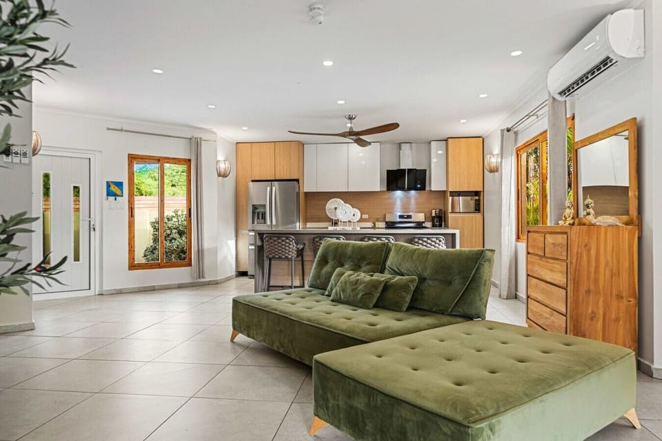 Bright natural light, sleek décor, and green velvet loungers give this living room a bold yet comfortable feel, perfect for conversation and downtime between outings