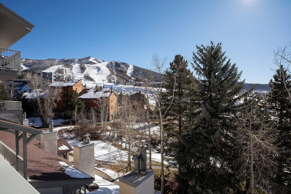 Mountain resort area with ski slopes visible in the distance, surrounded by lodges and evergreen trees during winter season.