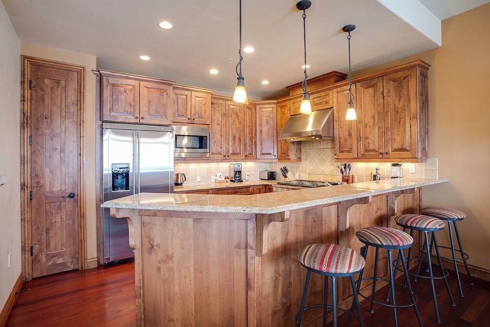 Gather around the spacious granite island in this warm, fully-equipped kitchen featuring rich wood cabinetry, stainless appliances, and stylish pendant lighting—your perfect space for morning coffee or preparing memorable meals together.