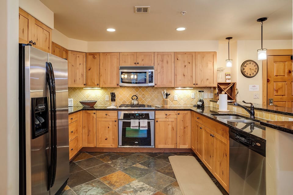 Your fully equipped kitchen features warm wood cabinetry, granite countertops, and stainless steel appliances—perfect for preparing meals or brewing morning coffee while settling in.