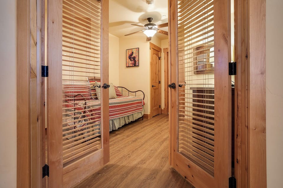 Step through rustic wood-slatted doors into your inviting bedroom, where warm tones and cozy bedding create a peaceful mountain retreat atmosphere.