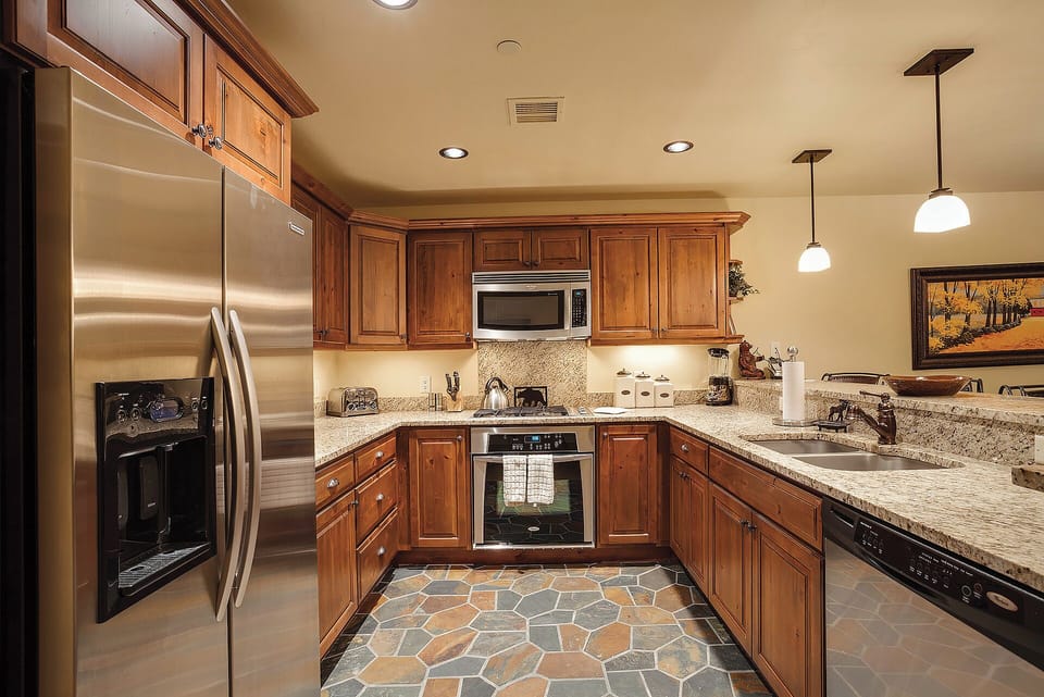Your fully equipped kitchen awaits with granite countertops, stainless appliances, and warm wood cabinetry. Picture yourself preparing meals on this spacious workspace, surrounded by natural light and elegant stone tile flooring.