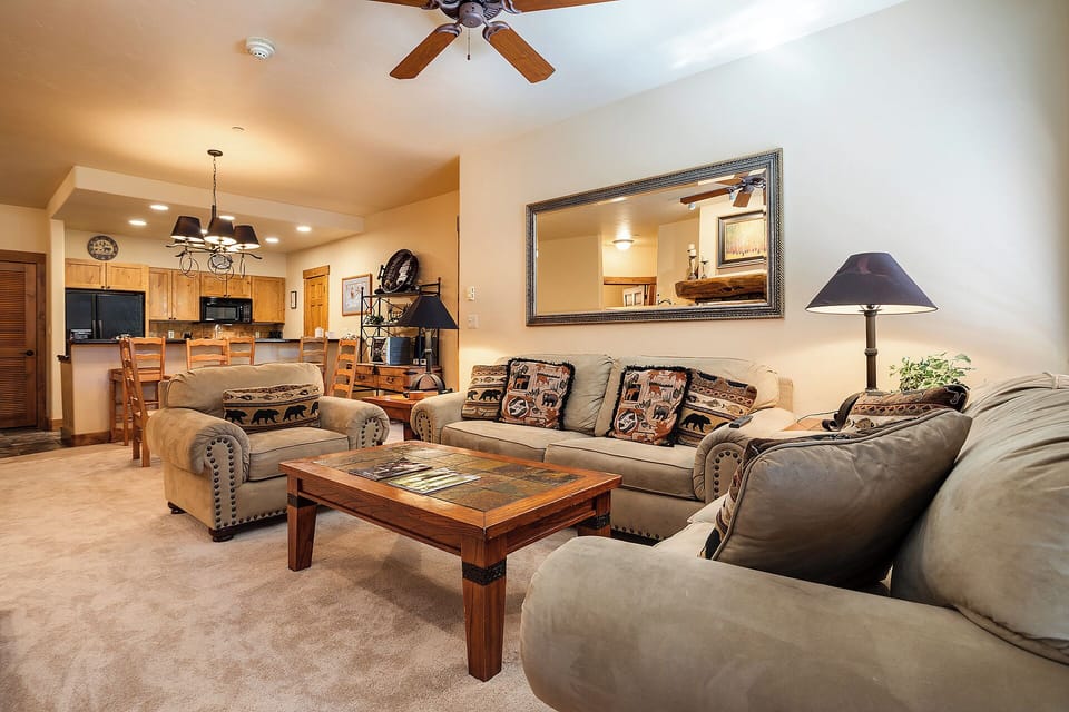 Sink into plush seating in your spacious living room, where rustic charm meets modern comfort with vaulted ceilings, a ceiling fan, and an open layout connecting to the dining area and fully equipped kitchen.