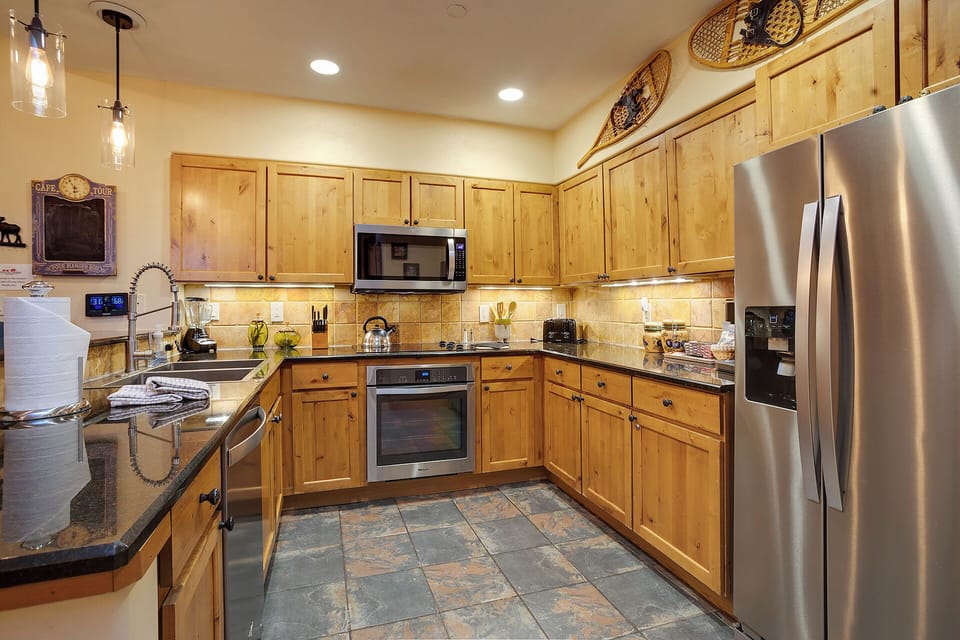 Your spacious kitchen features warm wood cabinetry, modern stainless steel appliances, granite countertops, and stylish lighting—perfect for preparing home-cooked meals during your mountain getaway.