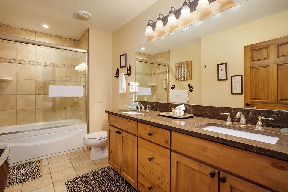 Your private bathroom retreat features a spacious double vanity with warm wood cabinetry, elegant granite countertops, a deep soaking tub, and a walk-in shower with beautiful tile work.
