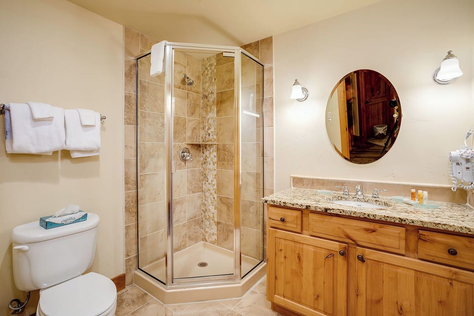 Your private bathroom features a luxurious walk-in shower with elegant stone tile, a spacious vanity with granite countertops, and warm wood cabinetry for storing all your essentials during your stay.