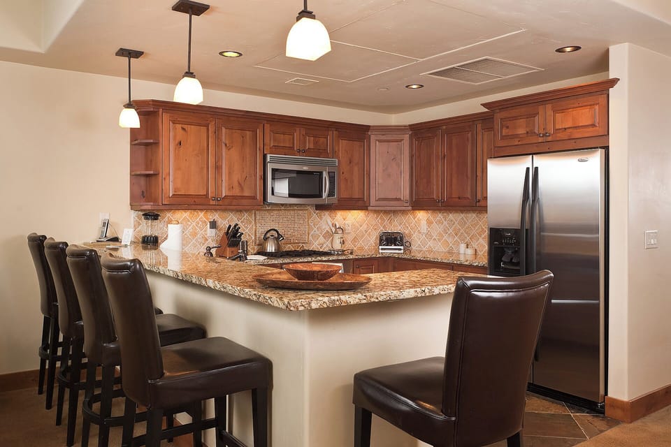 Your fully equipped kitchen features rich wood cabinetry, granite countertops, and stainless steel appliances—perfect for preparing meals together at the spacious breakfast bar.