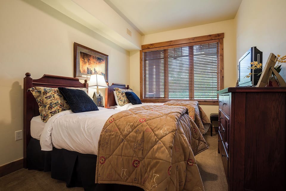 Settle into this inviting bedroom with plush bedding and charming rustic touches. Soft light filters through wood blinds while dresser space keeps your belongings organized for a relaxing mountain retreat.