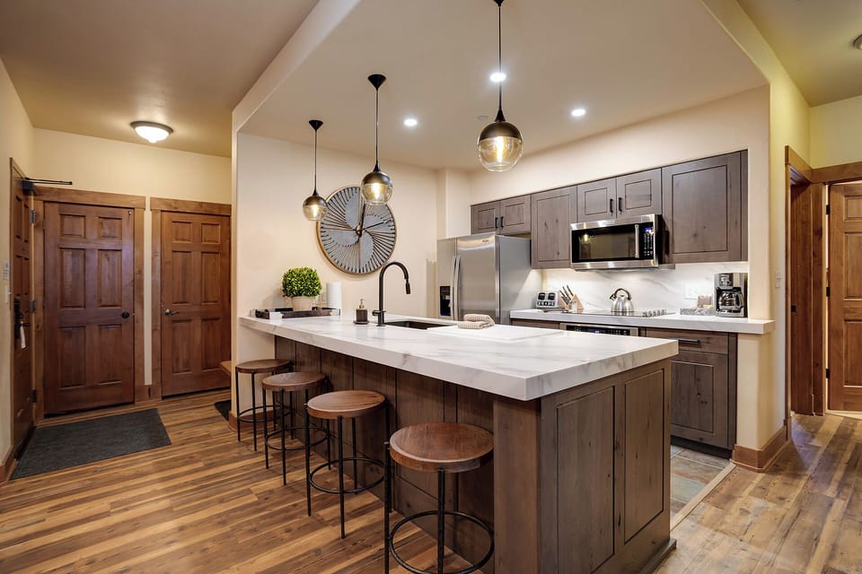 Modern kitchen with stylish island seating, stainless appliances, and warm pendant lighting—ready for your mountain getaway meals and morning coffee.