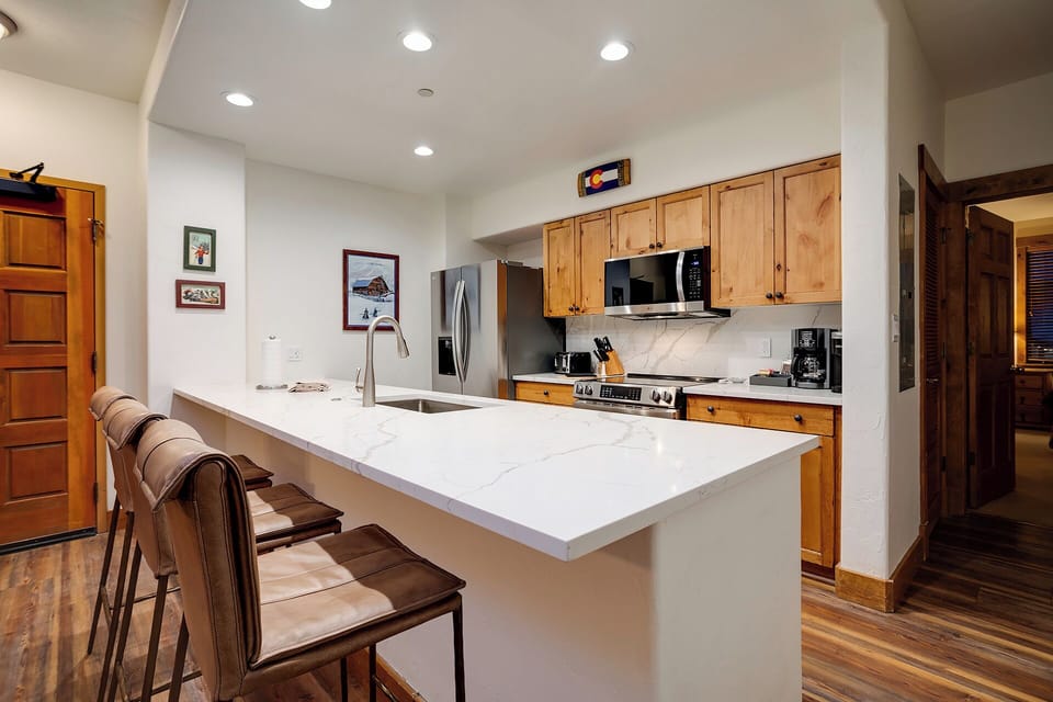 Your fully equipped kitchen features a spacious marble island with bar seating, stainless steel appliances, and warm wood cabinetry—perfect for preparing meals and gathering with loved ones.