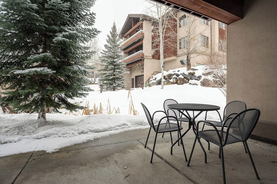 A covered patio overlooks a pristine winter landscape. This property is nestled among snow-draped evergreens, offering seasonal mountain charm and convenient access to nearby amenities.