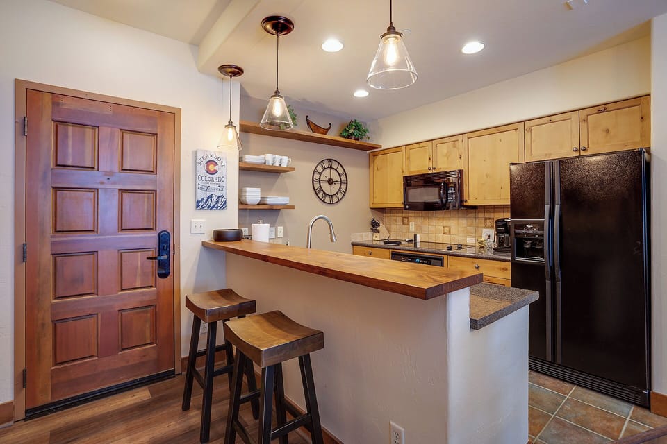 Step into your fully equipped kitchen with warm wood finishes, modern appliances, and a breakfast bar perfect for morning coffee or casual meals during your mountain getaway.
