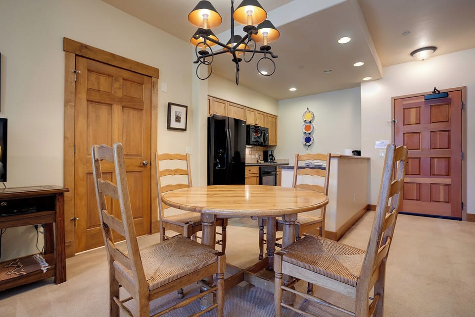 A welcoming dining space where you'll enjoy meals around a handsome wooden table, with a cozy chandelier above and a fully equipped kitchenette just steps away for your convenience.