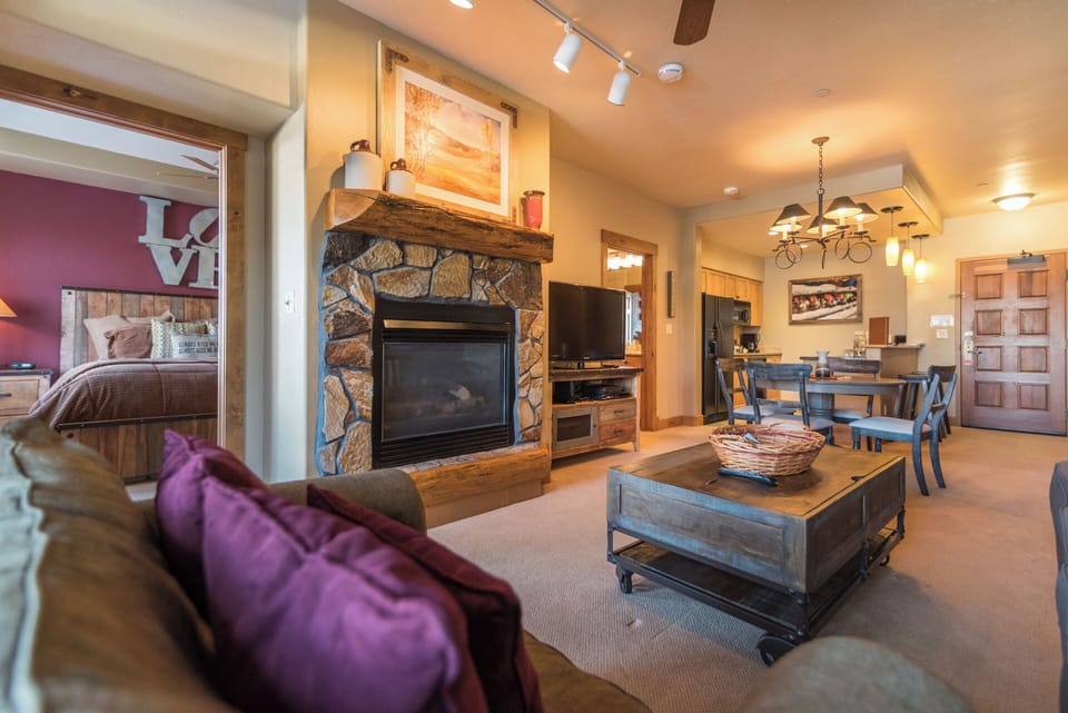 Unwind in your open living space with a stunning stone fireplace, rustic wood accents, and comfortable seating that flows into a cozy dining area and well-equipped kitchen.
