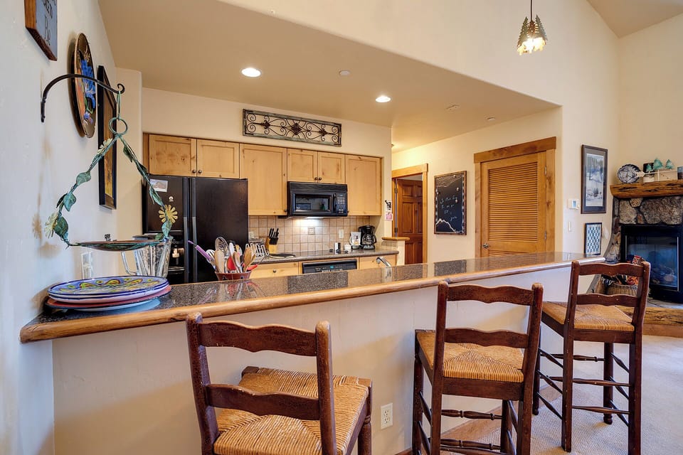 Gather around the breakfast bar in this inviting open kitchen, featuring granite countertops, modern appliances, and warm wood cabinetry—your perfect spot for morning coffee or casual meals during your stay.