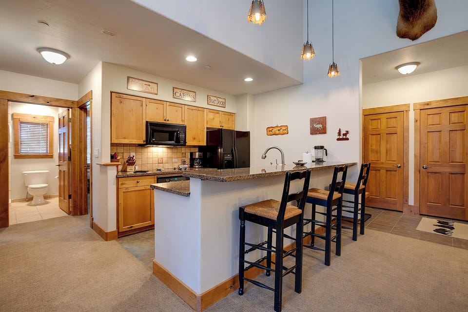 Gather around this inviting breakfast bar where warm wood tones meet mountain charm. Three stools await your morning coffee or evening appetizers, while pendant lights add a cozy glow to your culinary adventures.