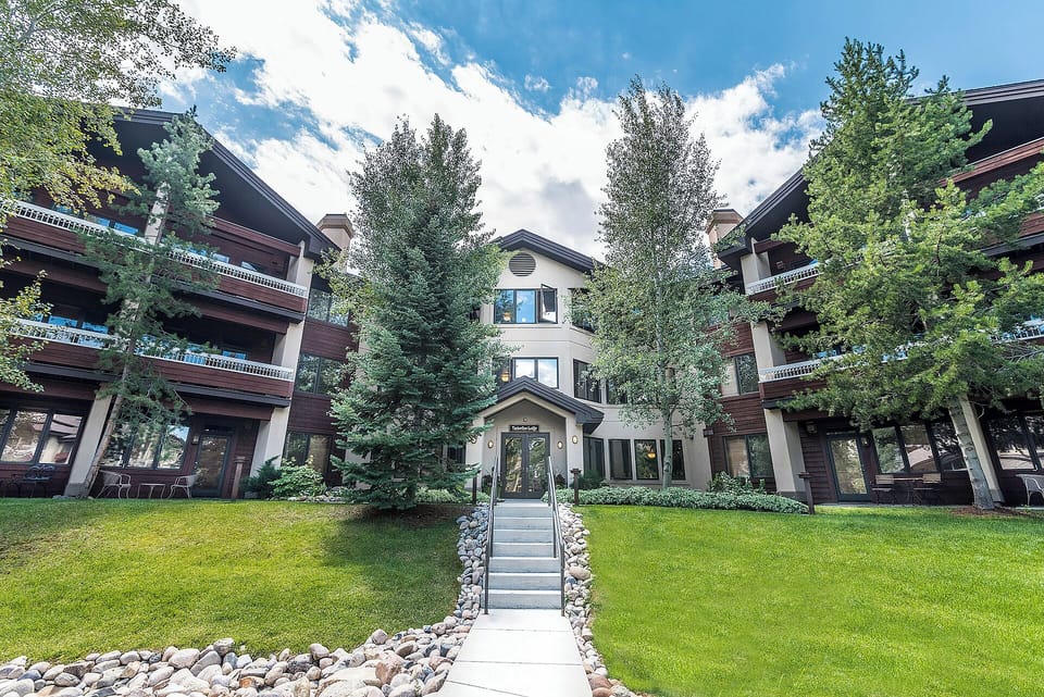 A multi-level property nestled among mature evergreens and landscaped grounds, offering a serene mountain retreat setting with convenient access and well-maintained exterior spaces.