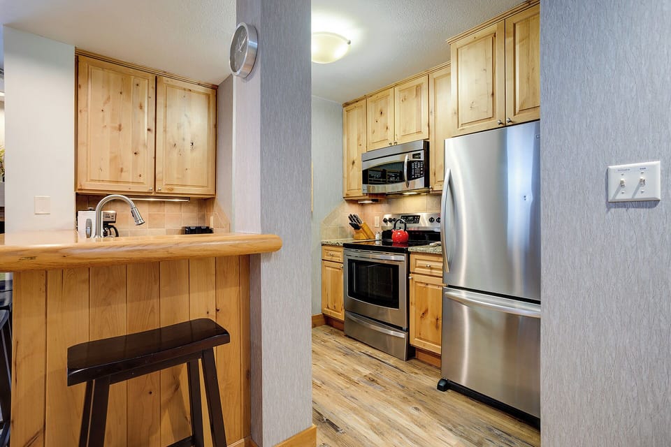 Your fully equipped kitchen features natural wood cabinetry, stainless steel appliances, and a convenient breakfast bar—perfect for preparing home-cooked meals or morning coffee during your stay.