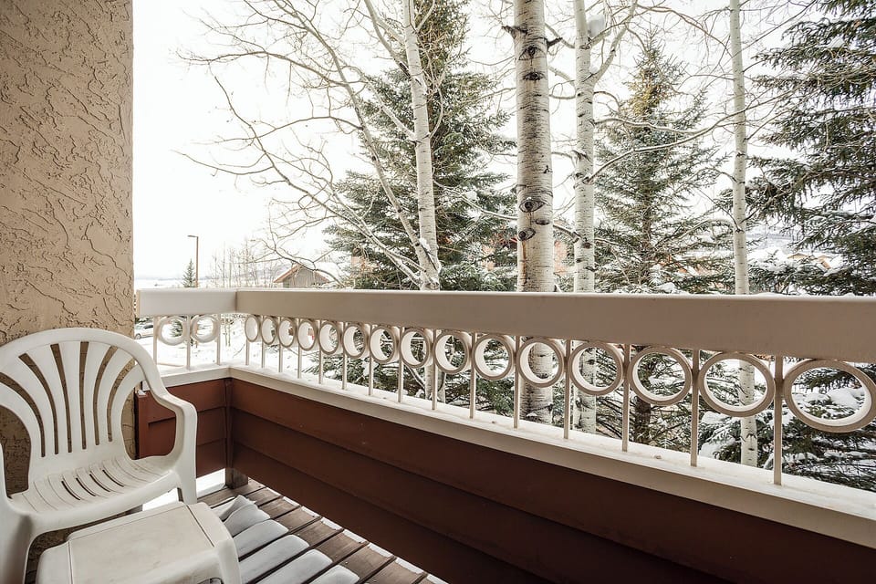 A peaceful balcony framed by towering aspens and evergreens, offering serene views of the surrounding winter landscape and a quiet space to unwind.