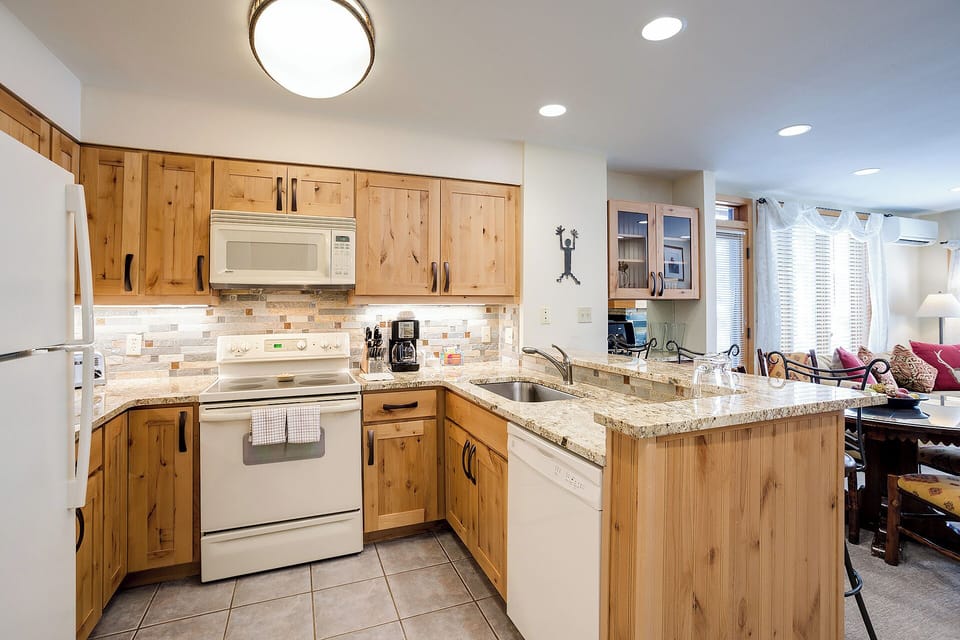 Your fully equipped kitchen awaits with natural wood cabinetry, granite counters, and modern appliances—perfect for preparing family meals or morning coffee before hitting the slopes.