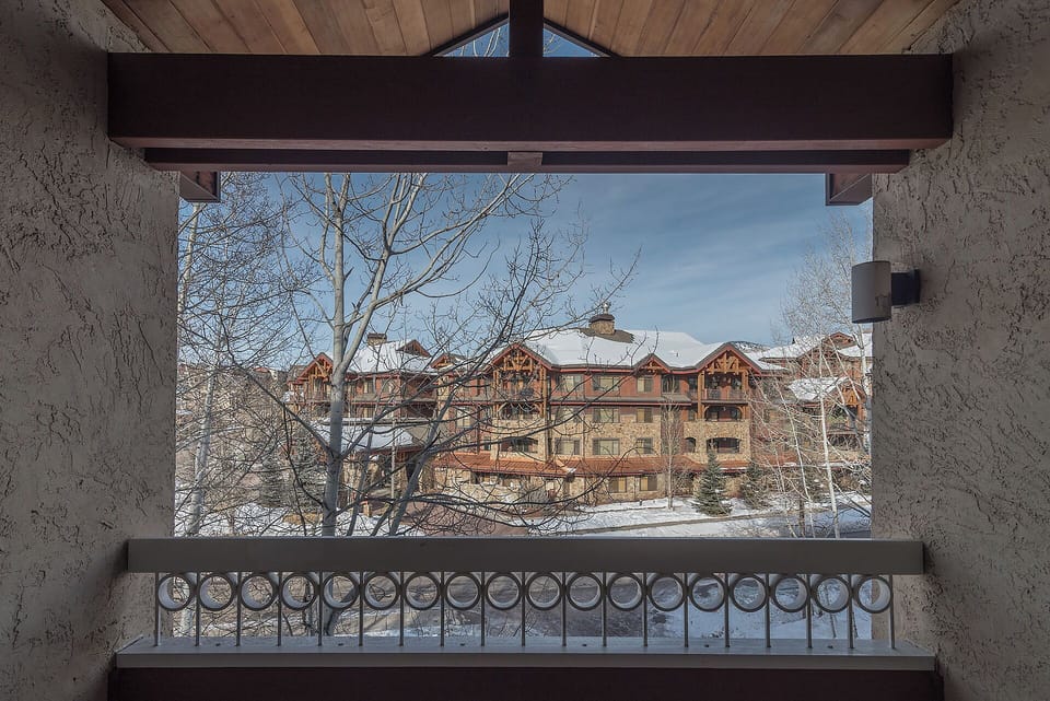 A picturesque winter scene of snow-covered timber-frame buildings framed by bare trees, set against a crisp blue sky in a serene mountain resort area.