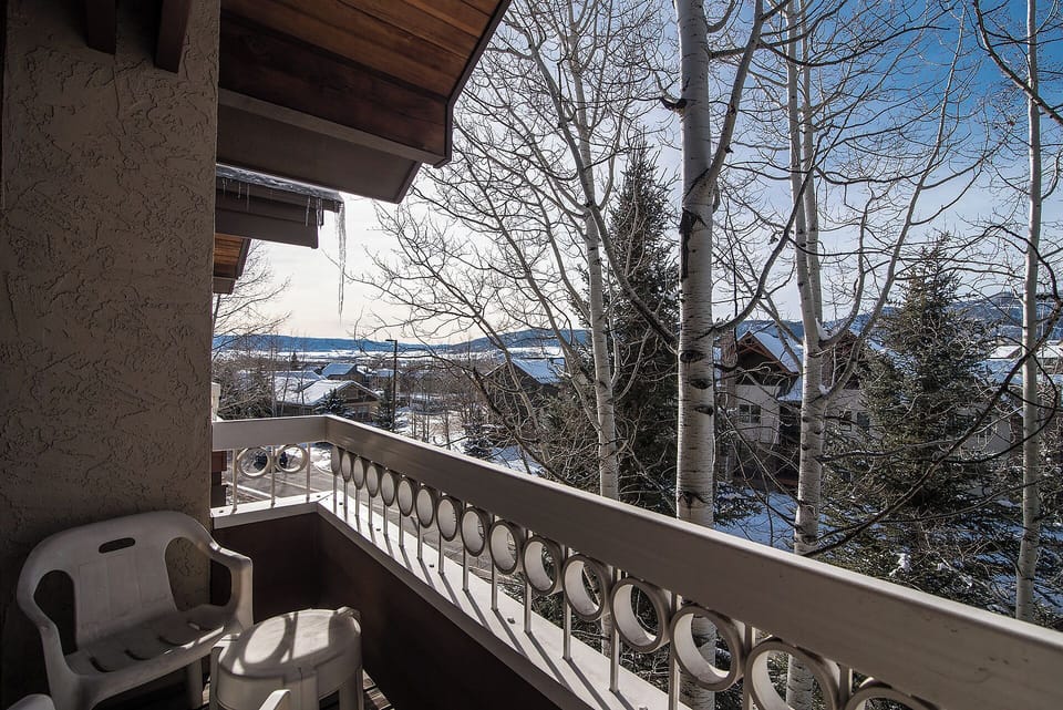 The balcony offers a peaceful view of the surrounding area with snow-dusted trees and neighboring buildings framing the distant hills, marking your arrival at this mountain retreat.
