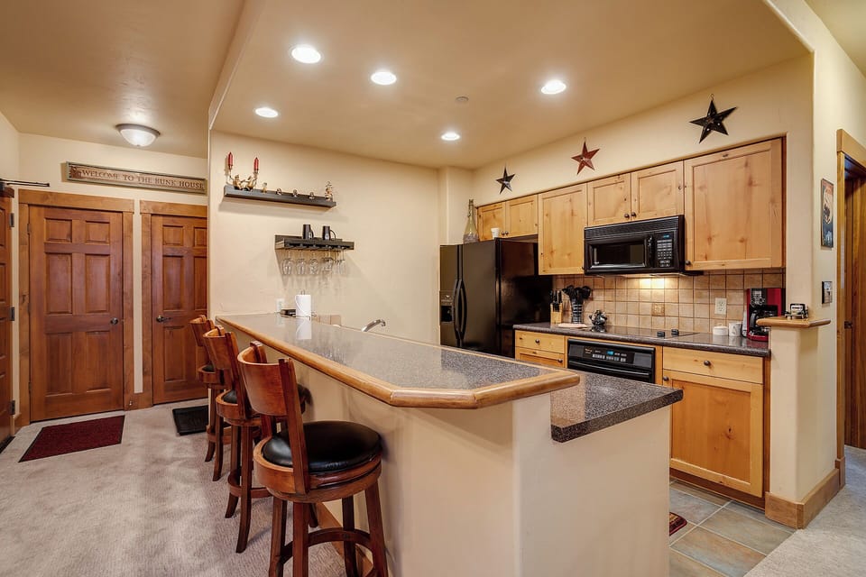 Step into your fully-equipped kitchen with modern appliances, warm wood cabinetry, and a spacious breakfast bar where you can gather for morning coffee or evening conversations in comfort.