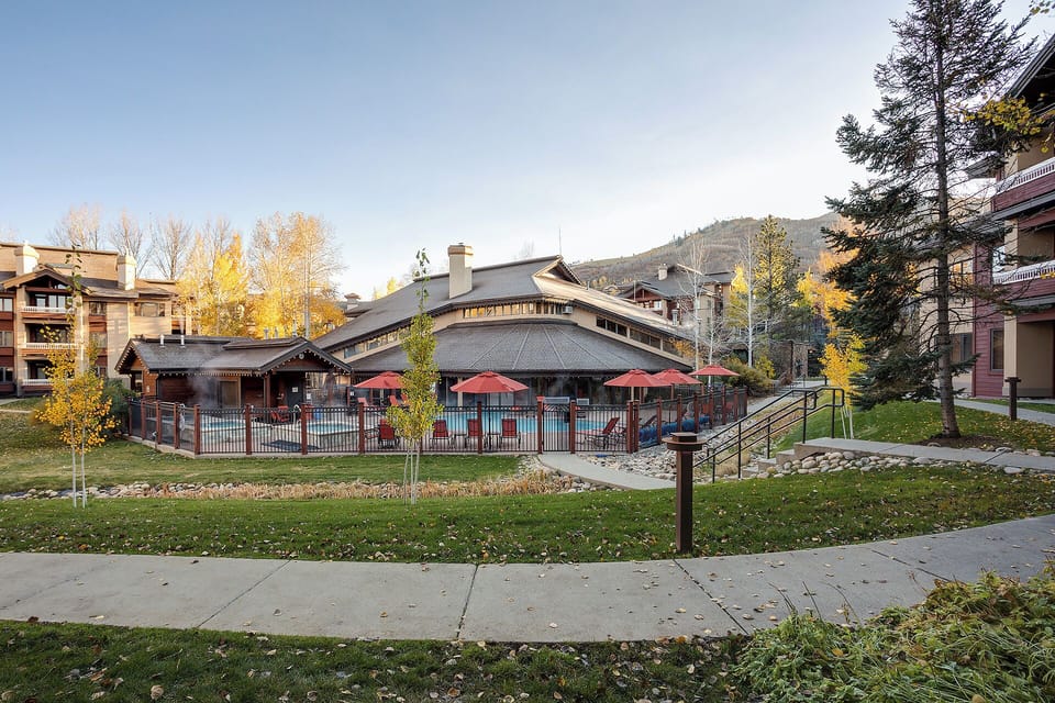 Resort-style pool with covered pavilion nestled in mountain surroundings, framed by autumn foliage and year-round evergreens in a quiet alpine neighborhood.