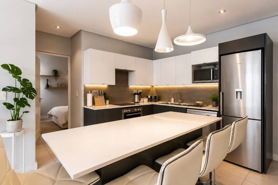 Kitchen: A contemporary kitchen with a generous breakfast island, cushioned stools, contrasting cabinetry, integrated appliances, pendant lighting, and extensive countertop space for cooking and dining.