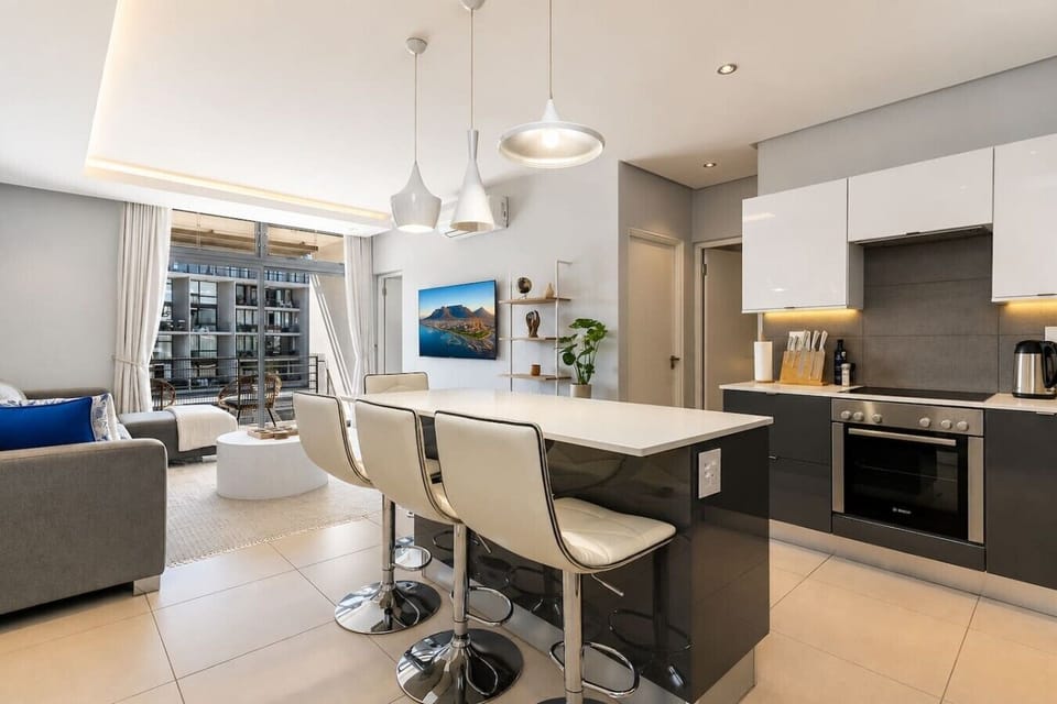 Full Kitchen: Sleek open-plan kitchen with glossy cabinetry, generous countertops, an integrated oven, and a spacious island with bar seating. Pendant lights add a polished touch, while the adjoining lounge creates an easy social flow.
