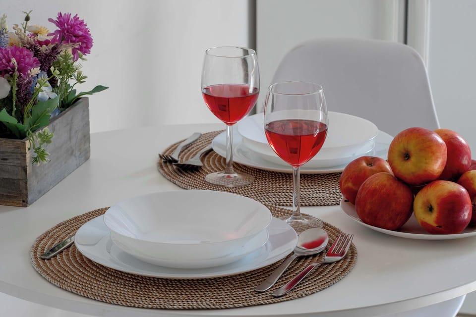 Elegantly arranged dining table with white plates, glasses of red wine, and fresh fruits.