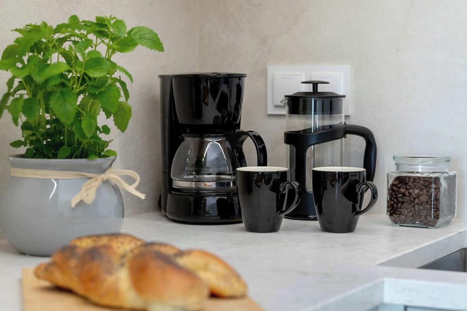 A kitchenette countertop featuring a coffee maker, another small appliance, a potted plant, and freshly baked bread. The light-colored decor creates a cozy and welcoming atmosphere.