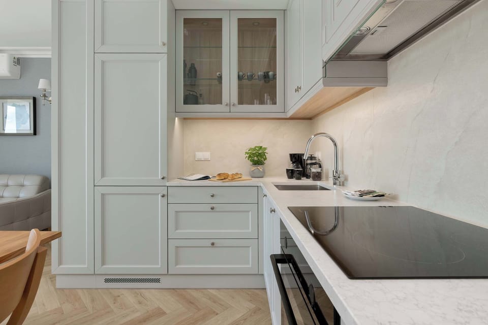 A modern white kitchenette with plenty of cabinets and a spacious countertop. Small appliances and decorative plants add practical and homely touches.
