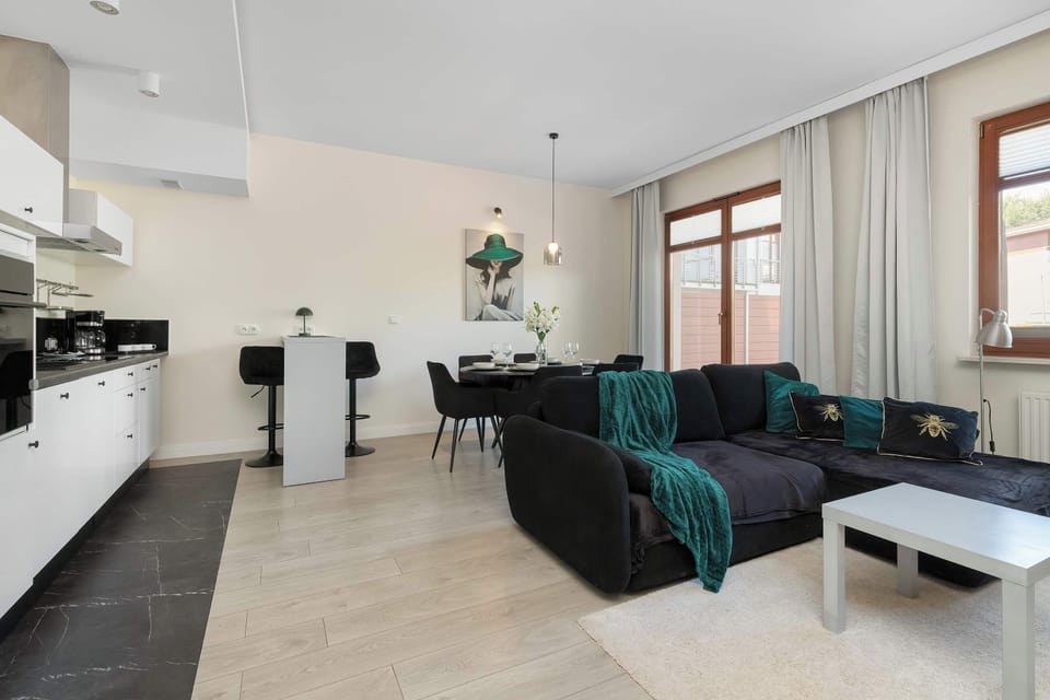 A bright living room with a comfortable sofa, TV, and dining area. Large windows provide plenty of natural light and a pleasant atmosphere.