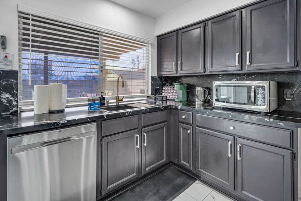 This sleek kitchen features dark cabinetry, marble-inspired countertops, and a touch of elegance with a gold-tone faucet. Stainless steel appliances and a cozy coffee bar corner complete the stylish, functional space.