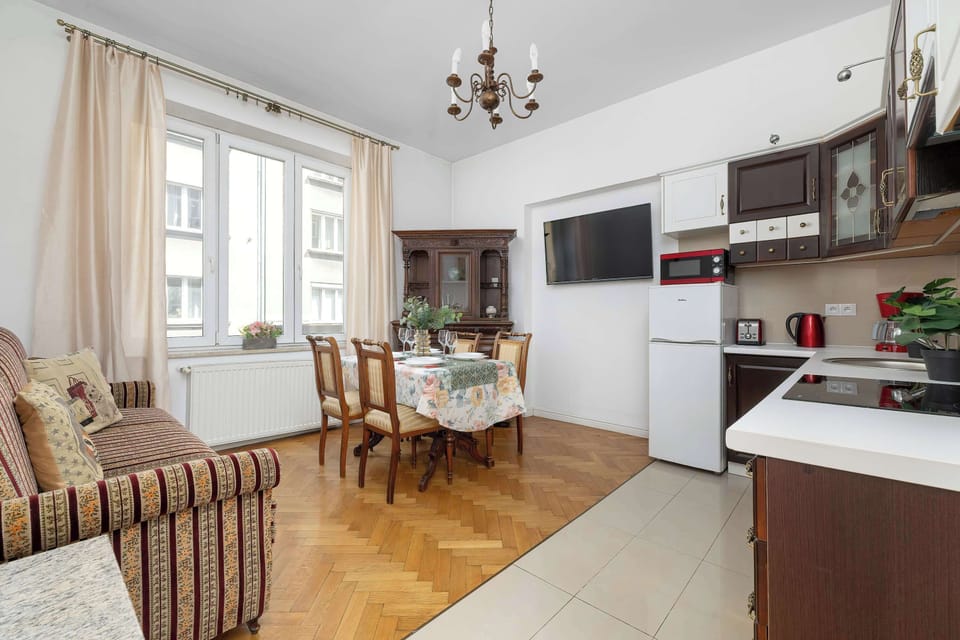 The dining and living space flows seamlessly into the kitchen area. A flat-screen television is mounted on the wall above the dining table, providing entertainment during meals.