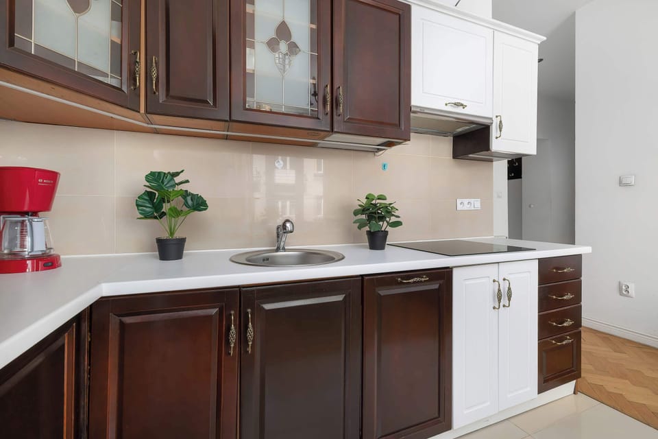 A modern kitchenette area boasts dark wooden lower cabinets and white upper cabinets. A red coffee maker adds a splash of color to the neutral countertops.
