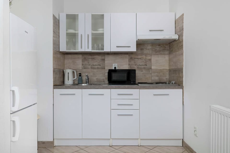A separate kitchen is fitted with white cabinetry and a beige tile backsplash. A freestanding white refrigerator stands on the left side.