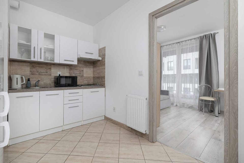 The kitchen view displays white upper and lower cabinets and tiled floors, with an open doorway looking into the adjacent room.