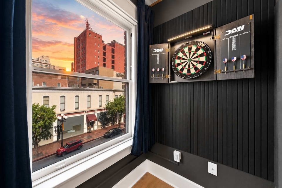 🎯 Dartboard on a dark accent wall beside a sunset window—a playful touch for game night in.