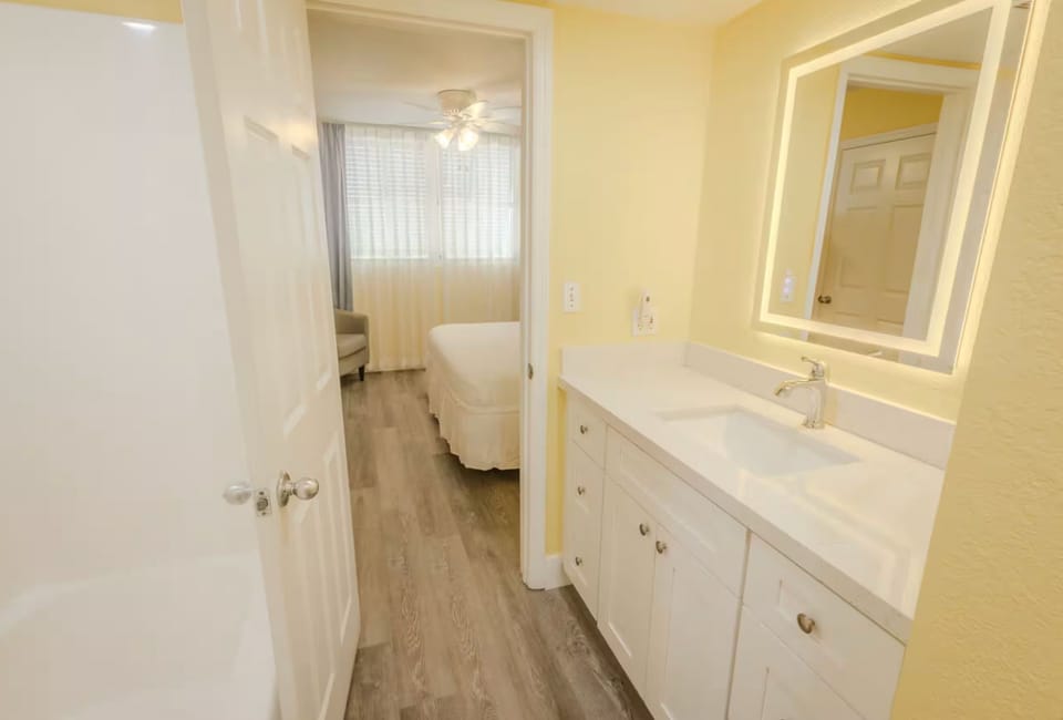 Bathroom featuring a white vanity and lit mirror, opening to the bedroom.