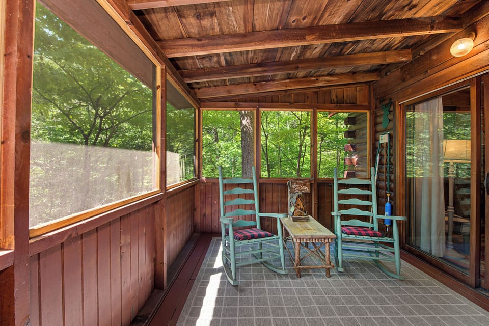 Step into your own screened porch retreat, where two rocking chairs invite you to unwind beneath rustic exposed beams. Surrounded by lush forest views, this cozy space feels like your private sanctuary for morning coffee or evening relaxation.