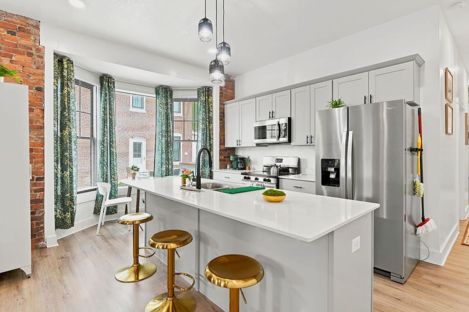 Cook meals in this modern kitchen featuring quartz countertops, stainless steel appliances, bar seating, and bright windows near downtown Fort Wayne attractions.