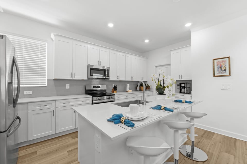 Your fully equipped modern kitchen features sleek white cabinetry, stainless steel appliances, and a bright island perfect for morning coffee or preparing family meals together.