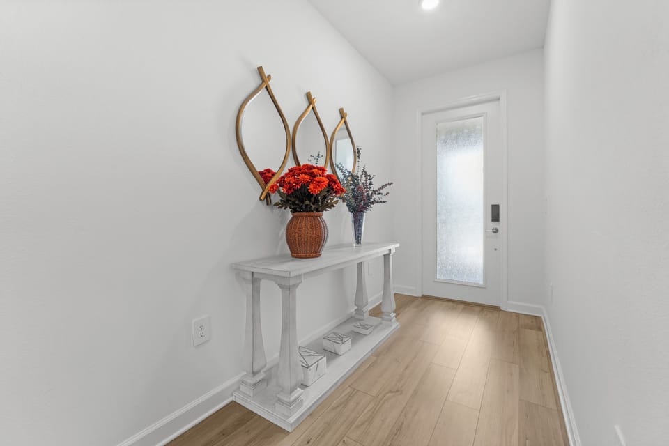 Step inside to a bright, welcoming entryway with light hardwood floors and crisp white walls. Fresh flowers add a warm, homey touch to your arrival.