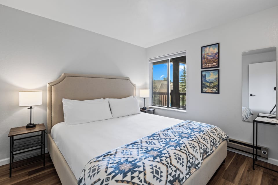 The bedroom offers a king size bed with an upholstered headboard and two end tables with lamps.