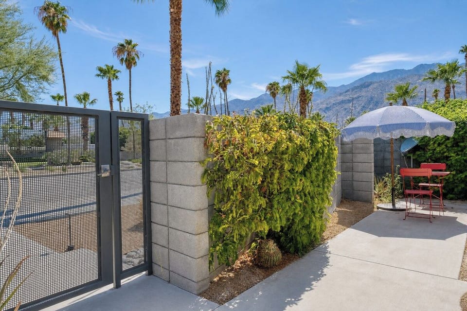 A private patio retreat framed by desert palms and mountain views, featuring a cozy bistro table shaded by an umbrella—your perfect spot for morning coffee or evening relaxation.