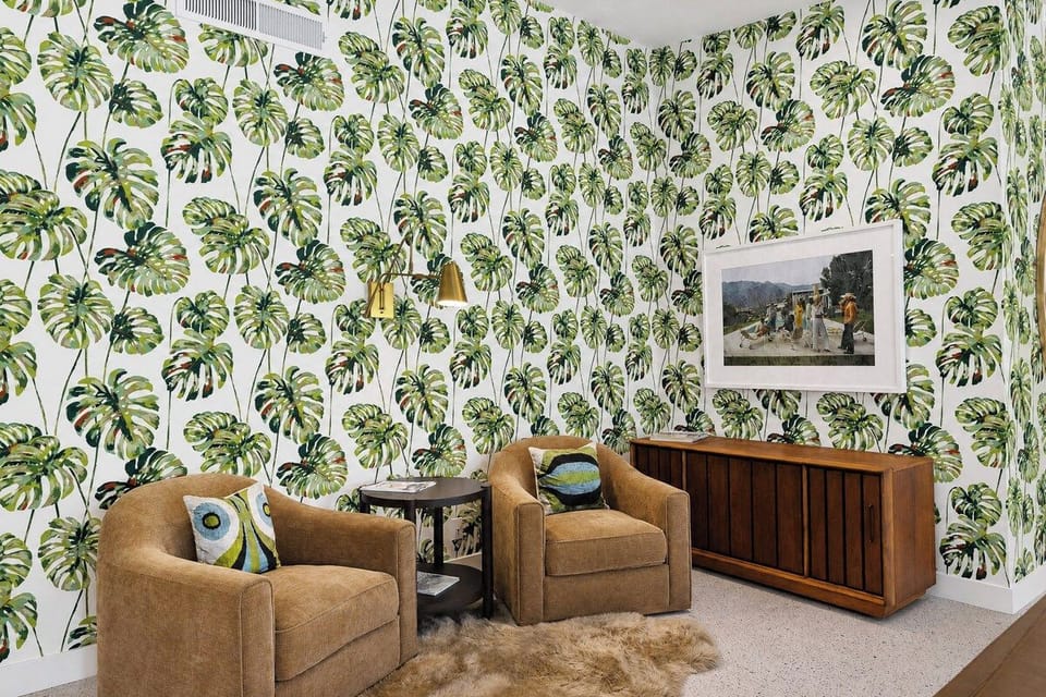 Relax in your stylish living space featuring lush botanical wallpaper, cozy armchairs, and warm wood tones that create a tropical, inviting atmosphere for unwinding after exploring.