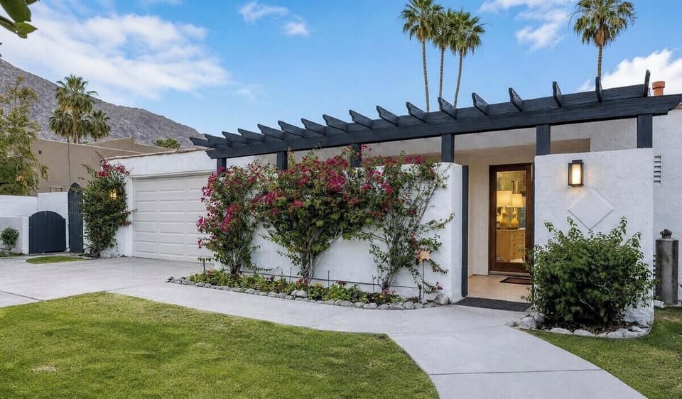 A modern desert retreat surrounded by lush landscaping and towering palms, set against mountain views in a peaceful Palm Springs neighborhood.